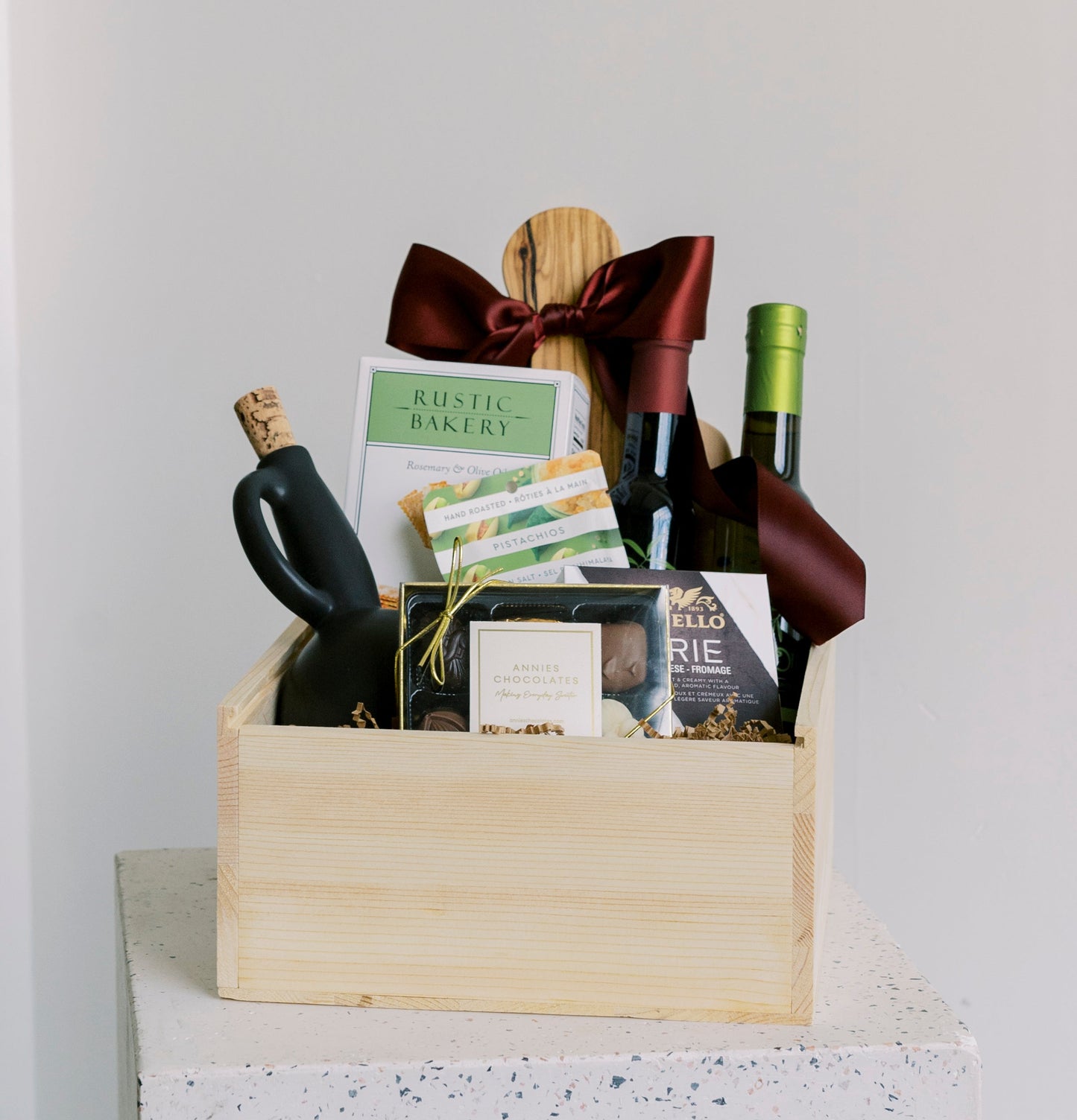 Wooden gift box with wine bottles, glasses, and a bow tie on a white surface.